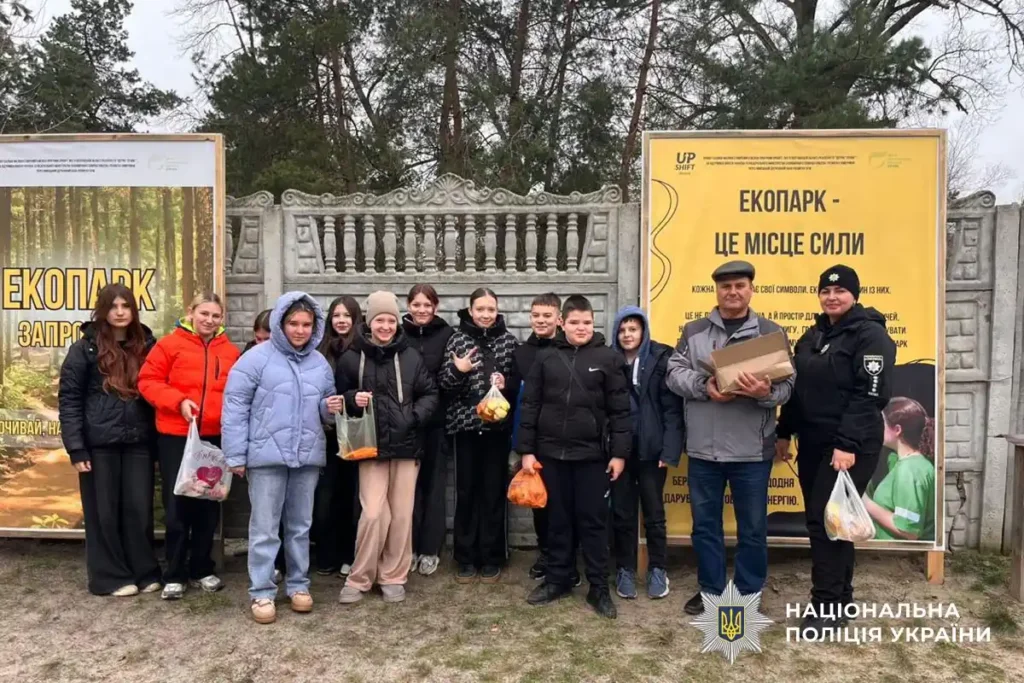 поліцейська з підопічними дітьми в екопарку біля входу, тримають у руках смаколики для тварин