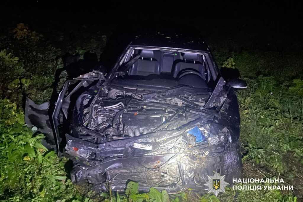 на траві стоїть вщент зім'ятий темний легковий автомобіль