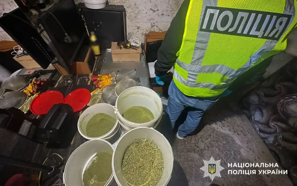 людина в жилеті з написом поліція в приміщенні біля відер із подрібненими сухими рослинами